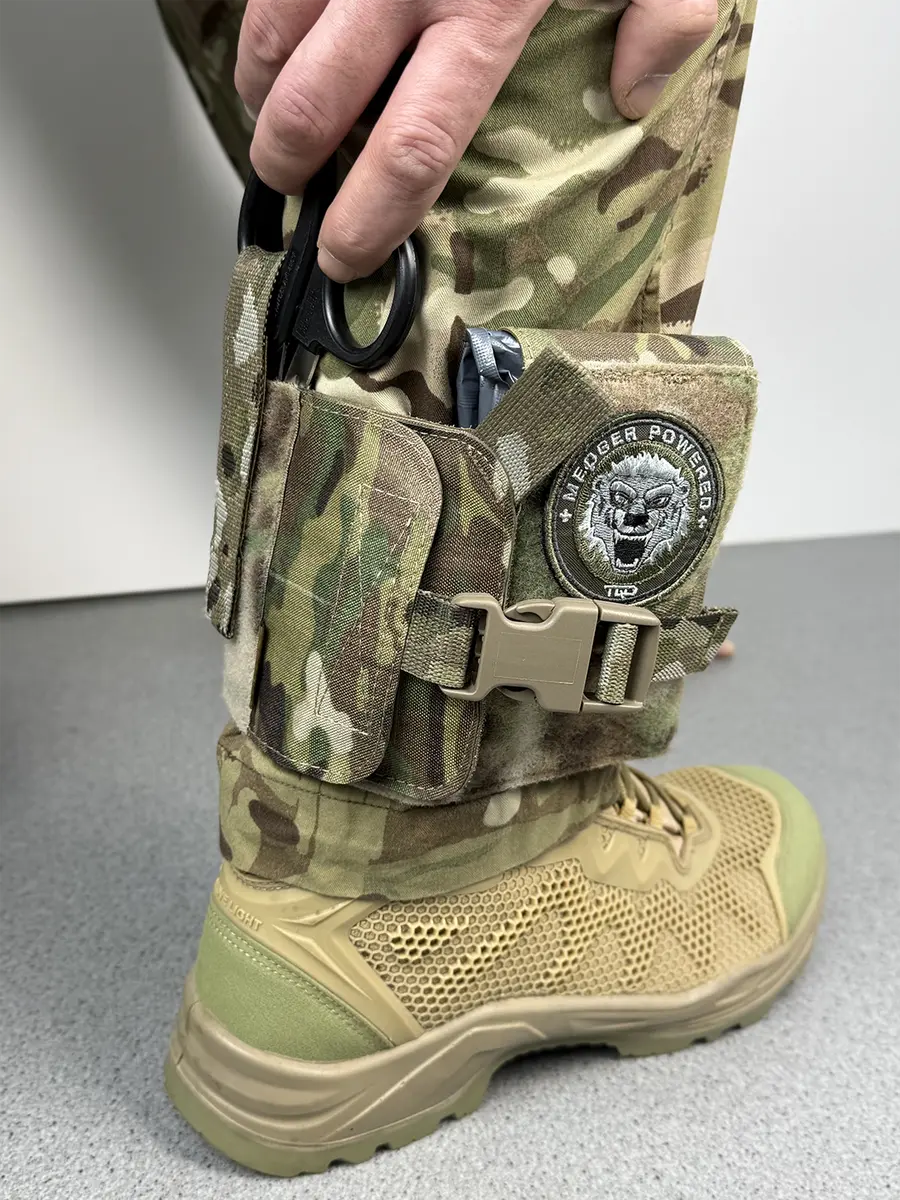 Operatore che estrae rapidamente le forbici di emergenza dalla custodia IFAK da caviglia tattica DNIPRO PM23 in Multicam durante una simulazione operativa.